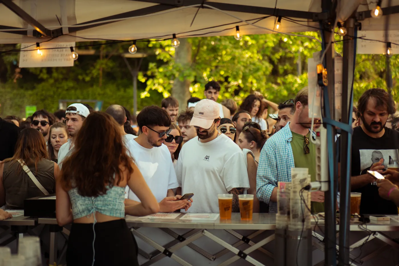 La file devant le bar en plein air, pintes de bière artisanale sur le comptoir et guirlandes lumineuses
